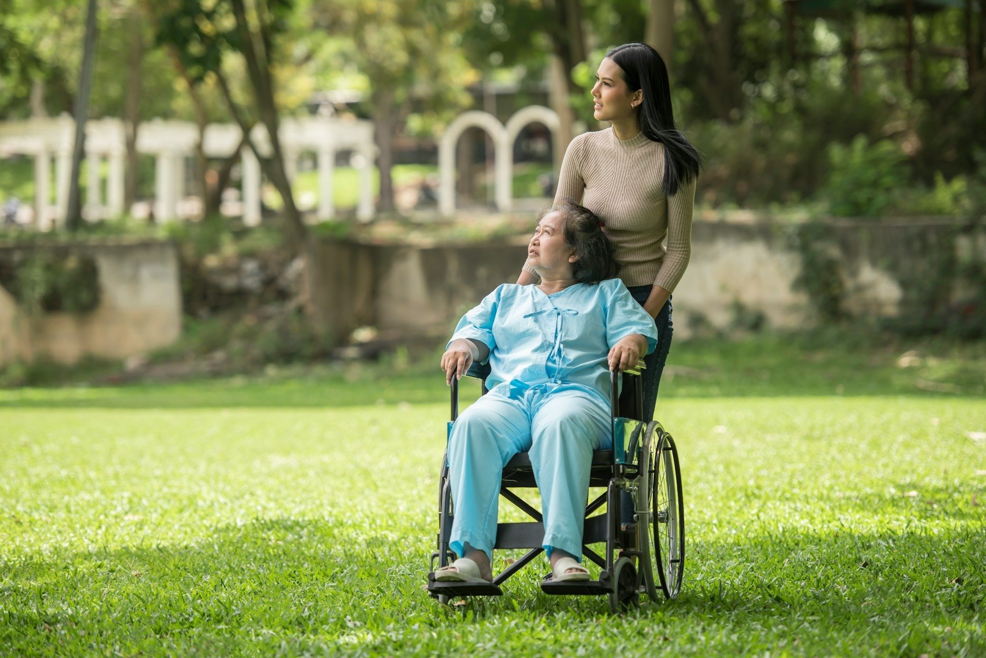 Caregiver pushing a wheelchair along a path through a park