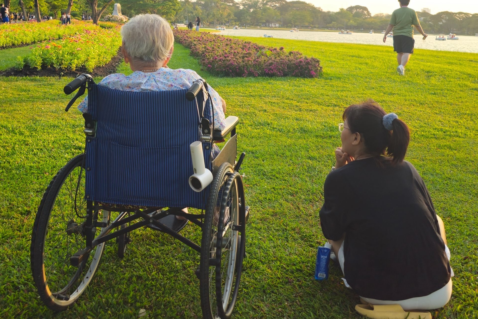 Companion sitting beside a wheelchair user in a garden at sunset