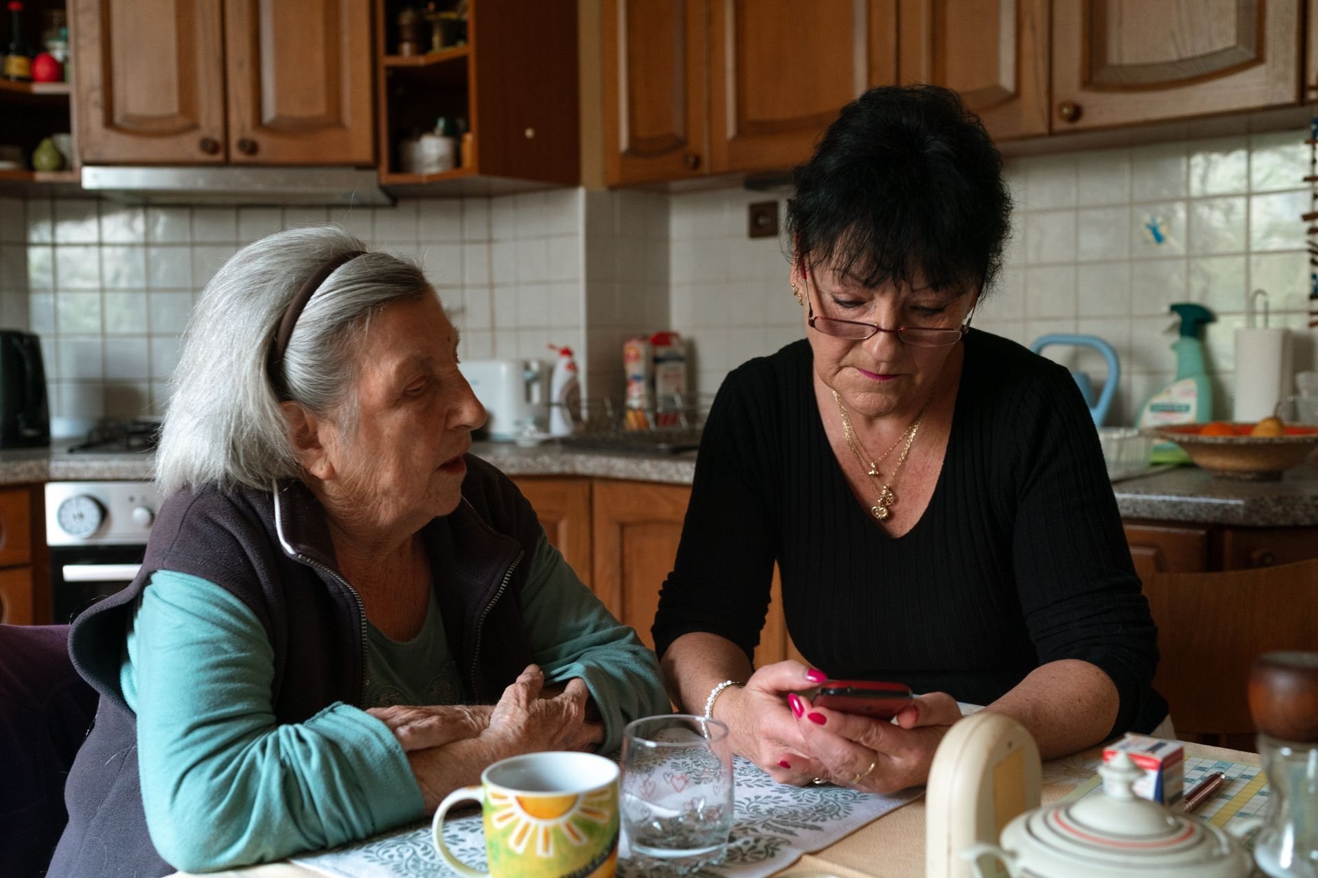 Caregiver sitting with an older woman at her kitchen table, phone in hand