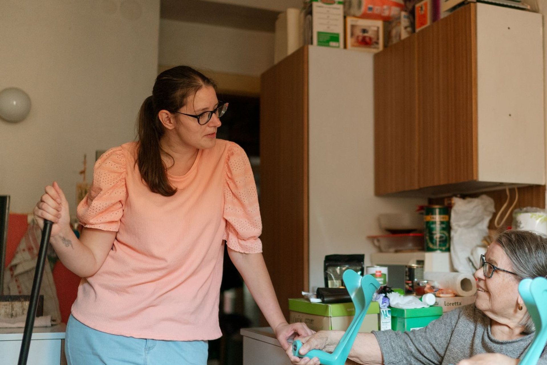 Caregiver talking with an older woman in her kitchen, crutches within reach