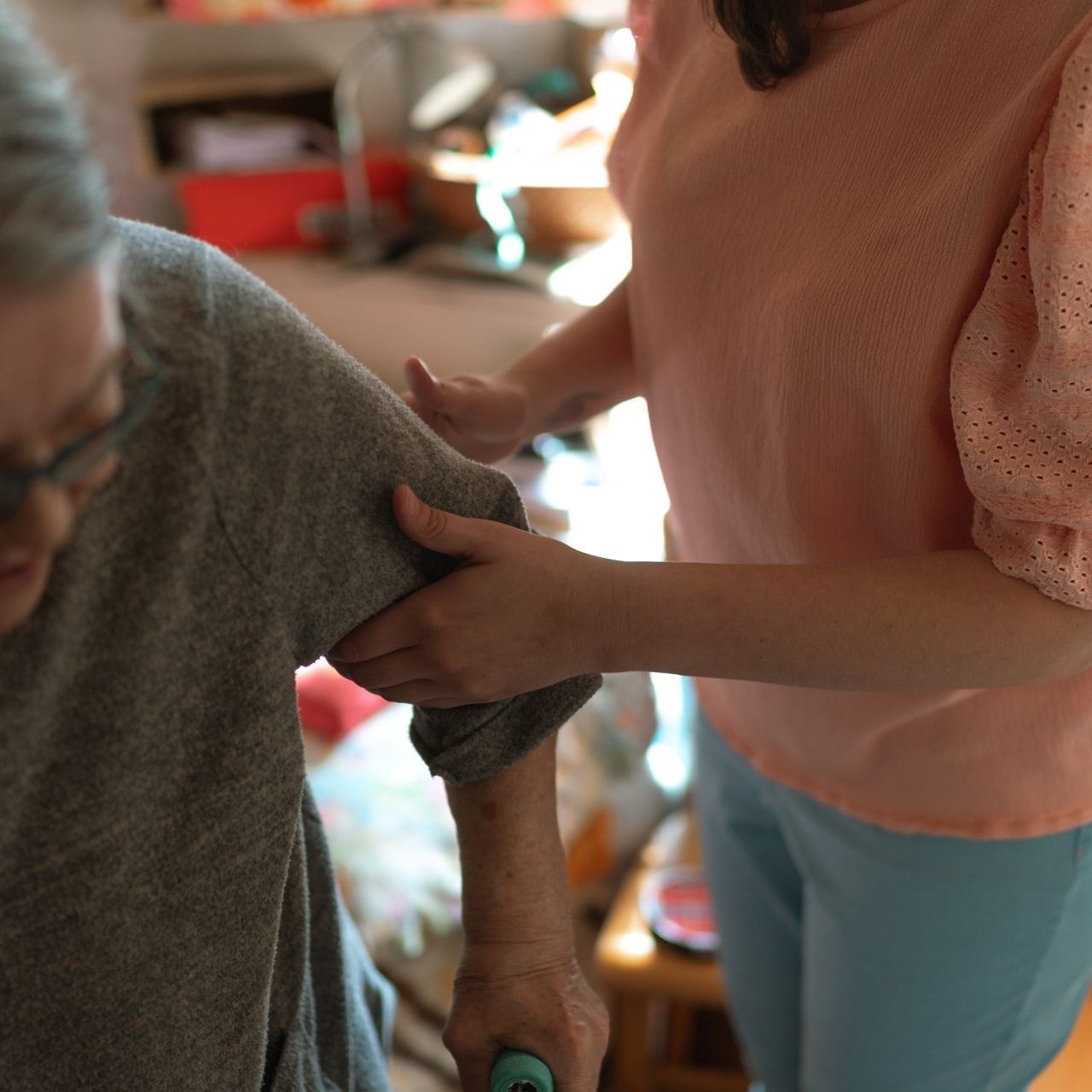 Caregiver easing an older woman’s arm into her sleeve