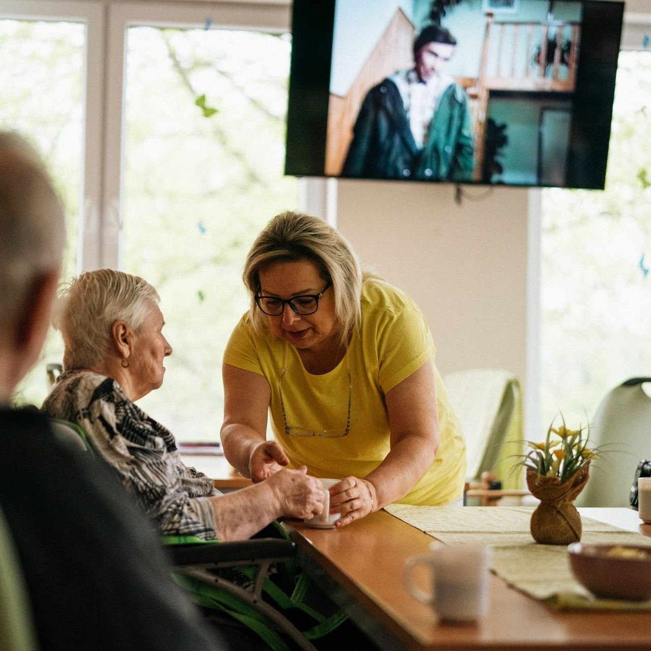 Caregiver bringing a warm drink over to an older woman