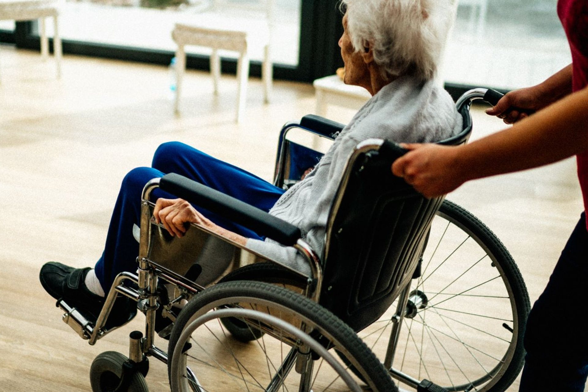 Caregiver pushing an older woman’s wheelchair through a bright room